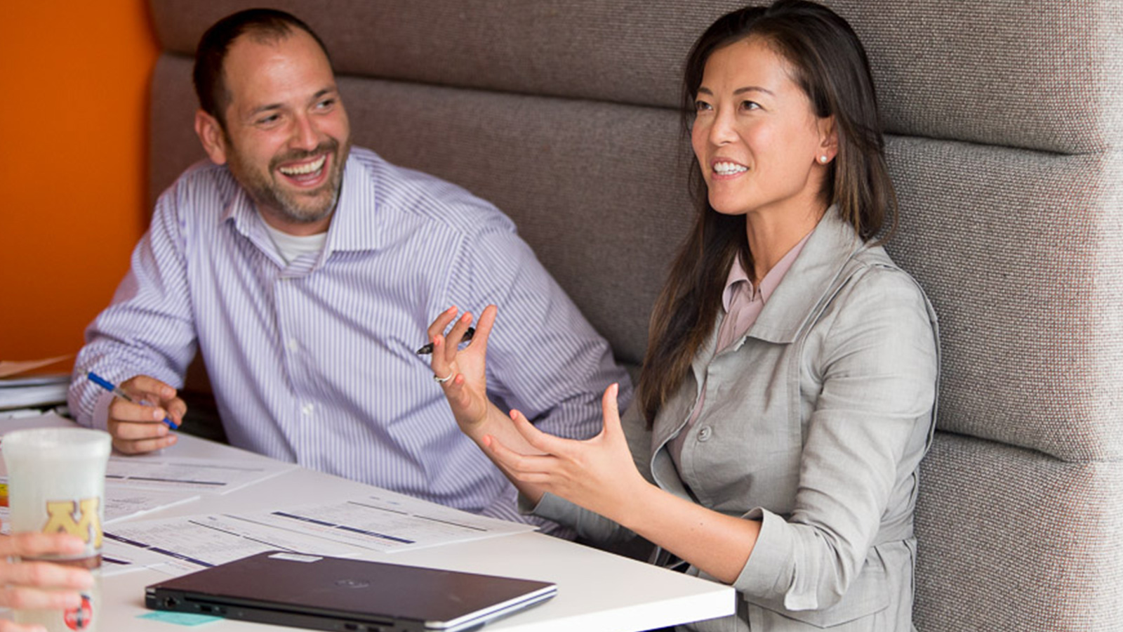 Man and woman at table with closed laptop discussing document. Man and woman at table with closed laptop discussing document.