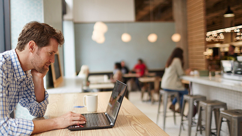 A man sitting in a coffee shop performing an online transaction on his laptop. A man sitting in a coffee shop performing an online transaction on his laptop.
