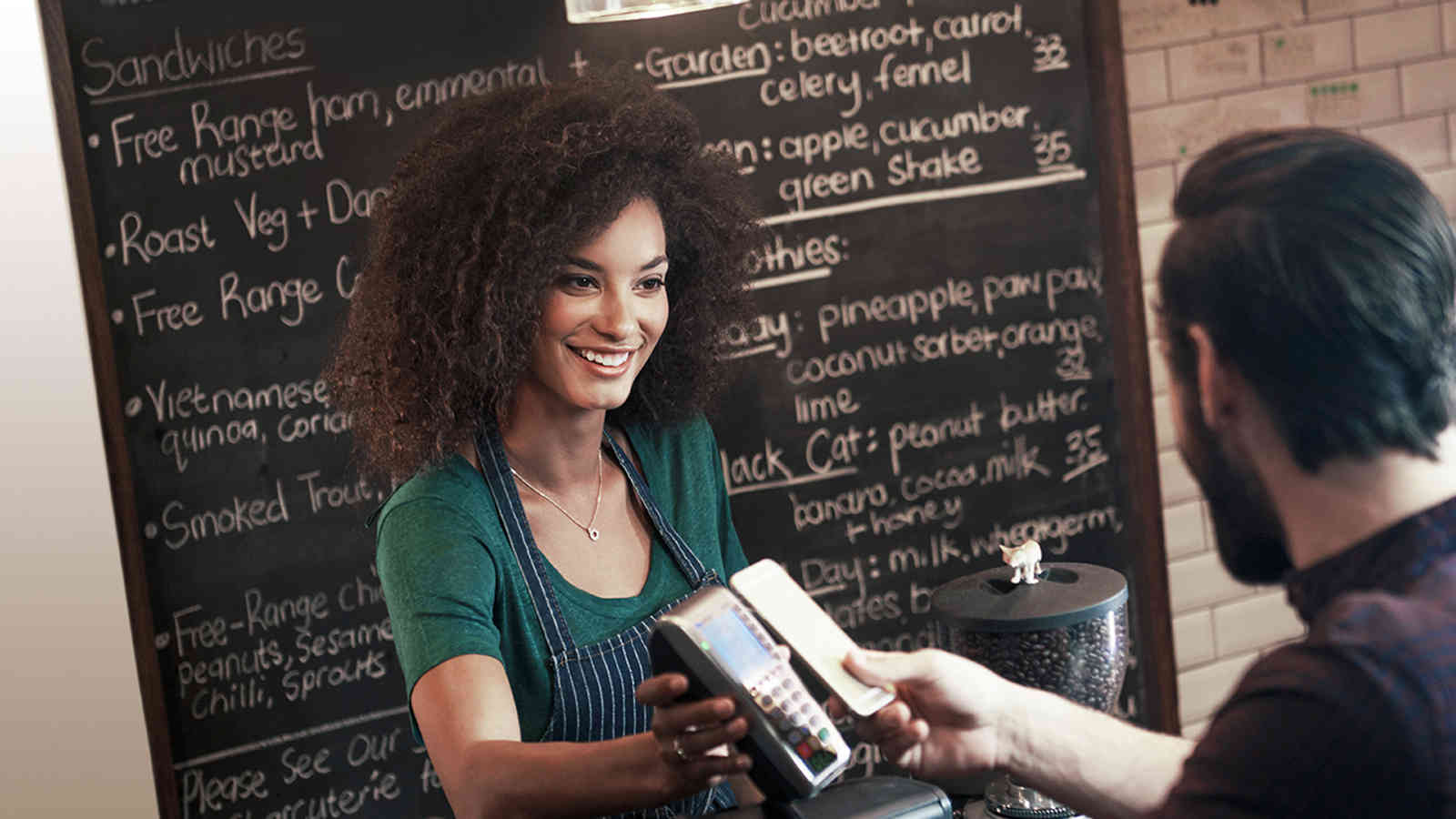 Woman holding a payment terminal for a man who is making a contactless mobile payment.