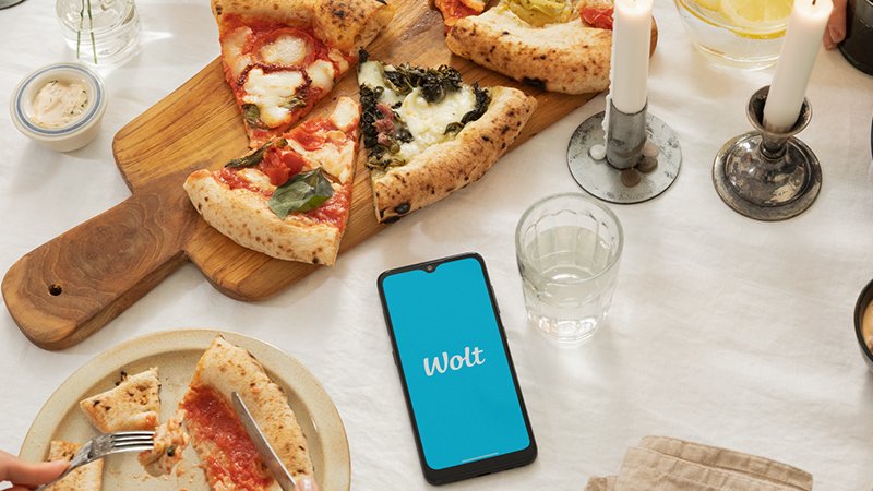 wolt logo on phone next to served pizza